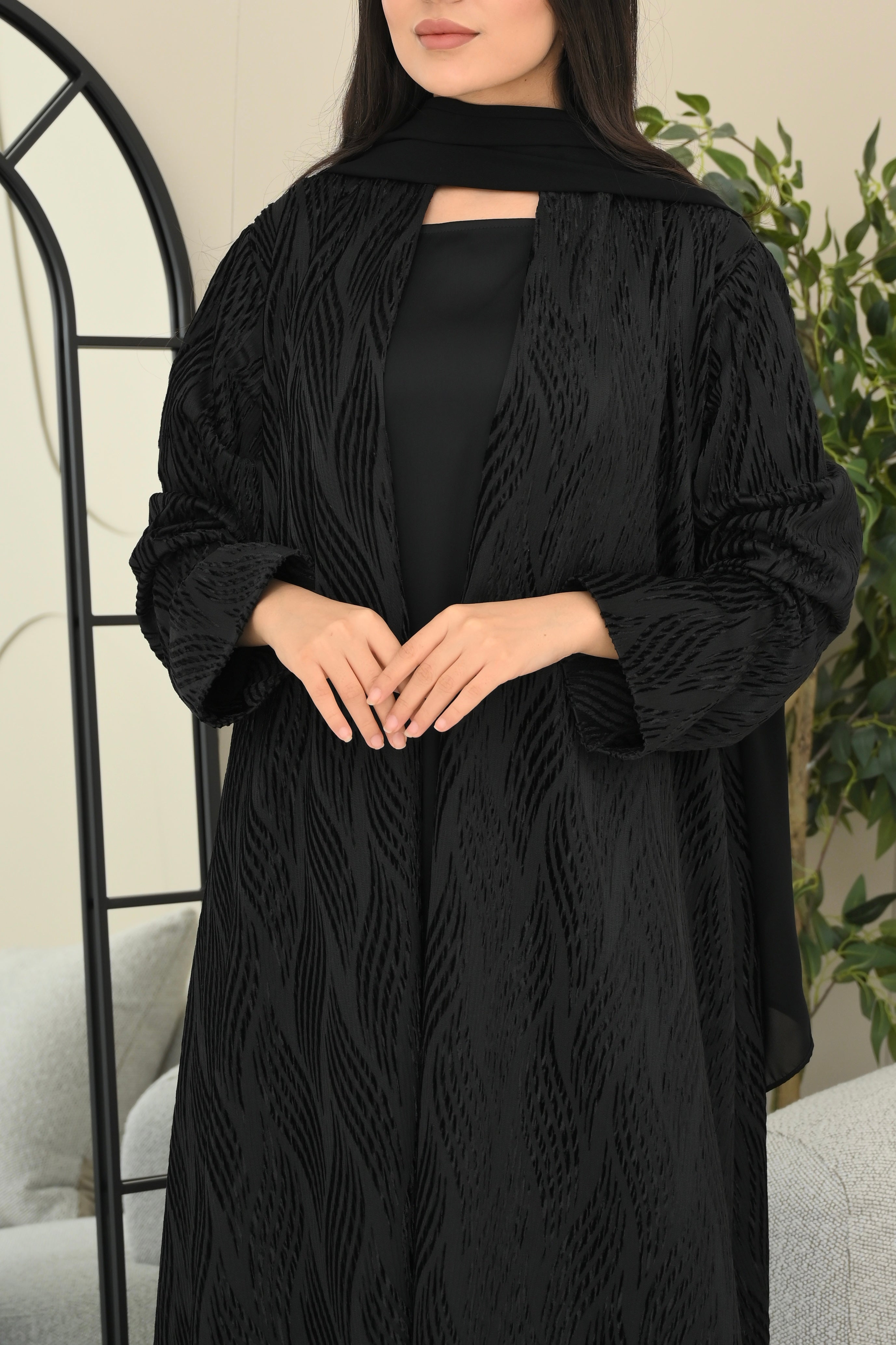 Woman wearing a black abaya with intricate detailing in a neutral setting.