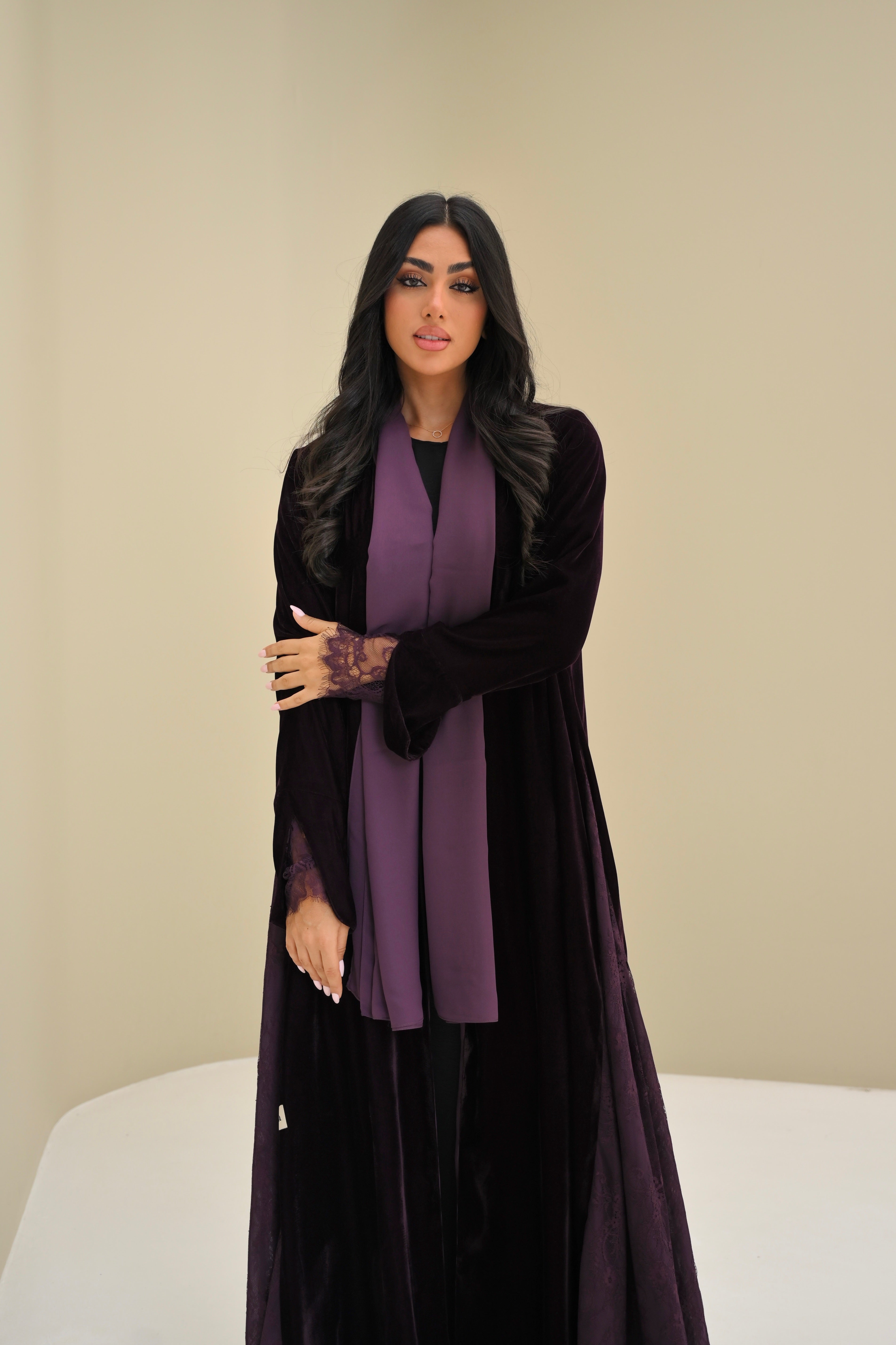 Woman wearing a black abaya with a purple scarf against a beige background