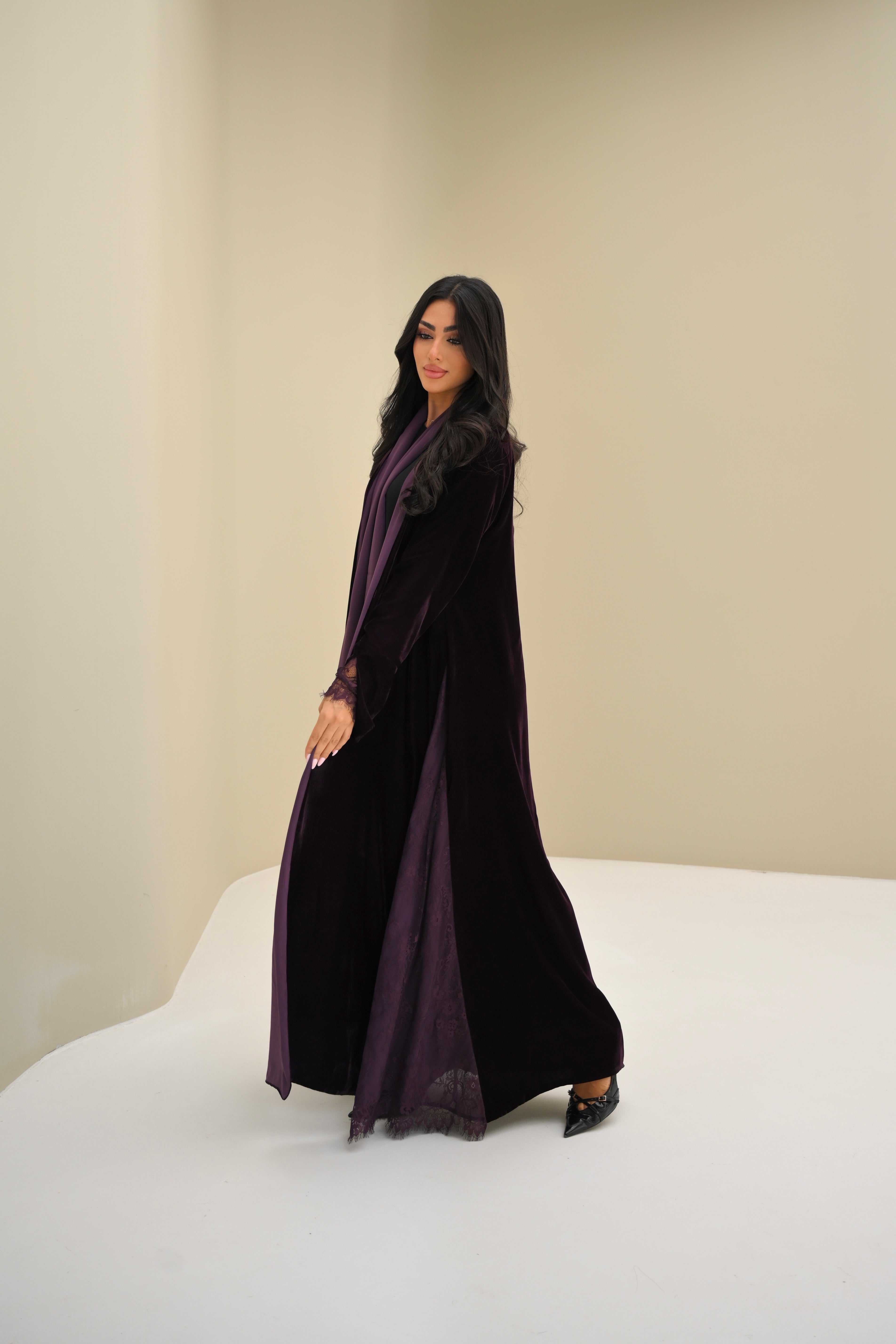 Woman wearing a long black dress with a purple scarf against a beige background