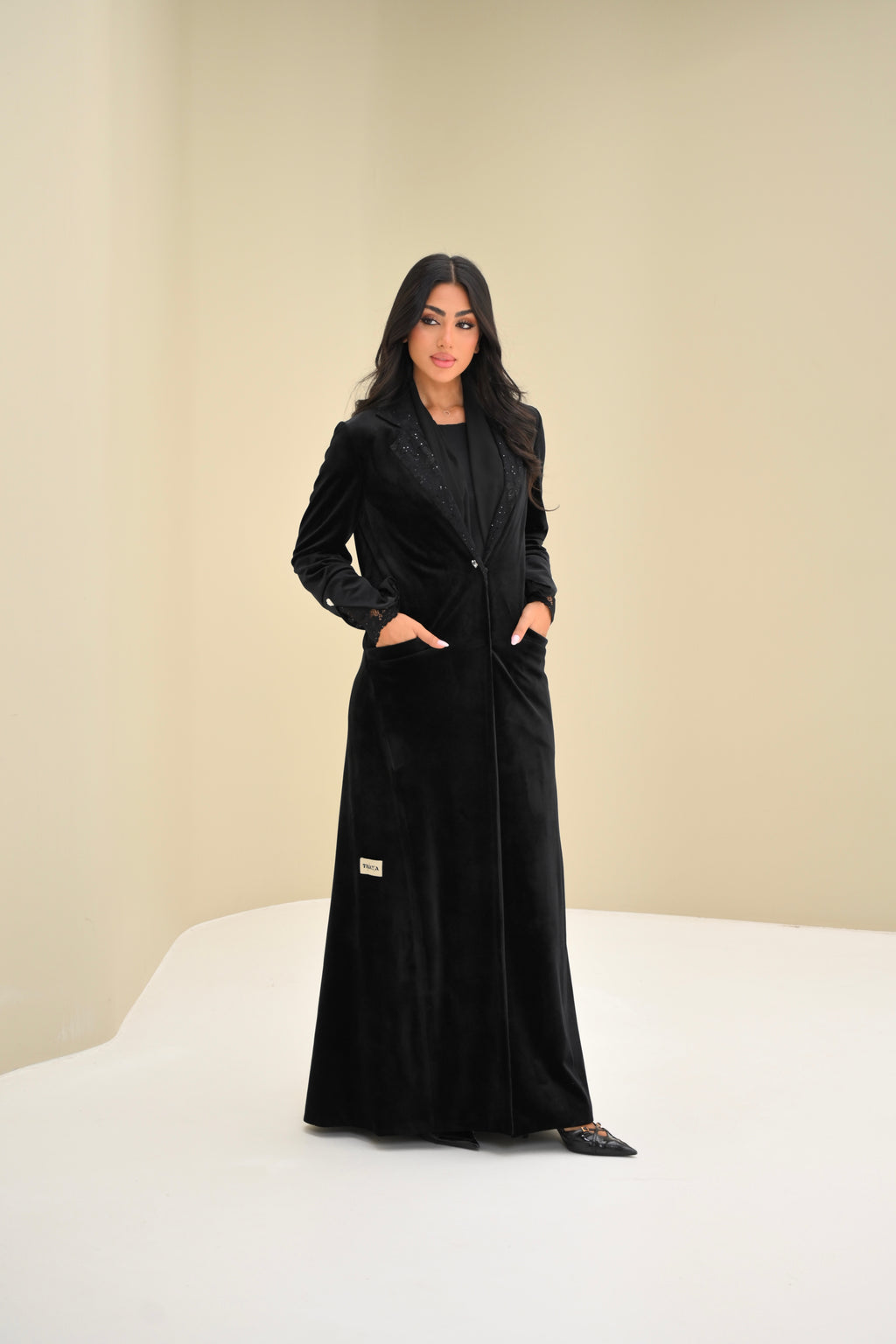 Woman wearing a black coat standing on a white surface with a beige background