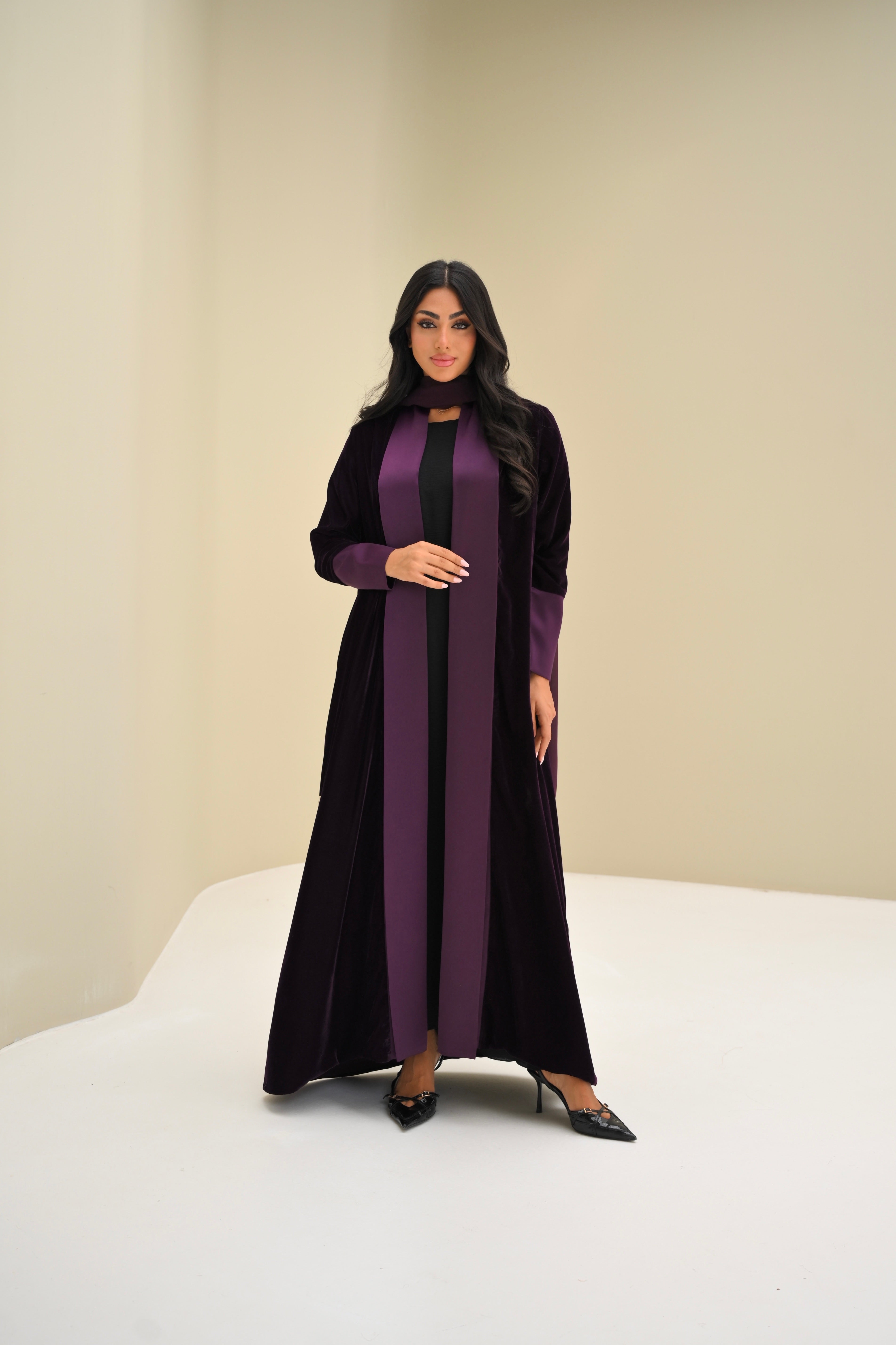 Woman wearing a long, dark purple dress with a high collar against a plain background