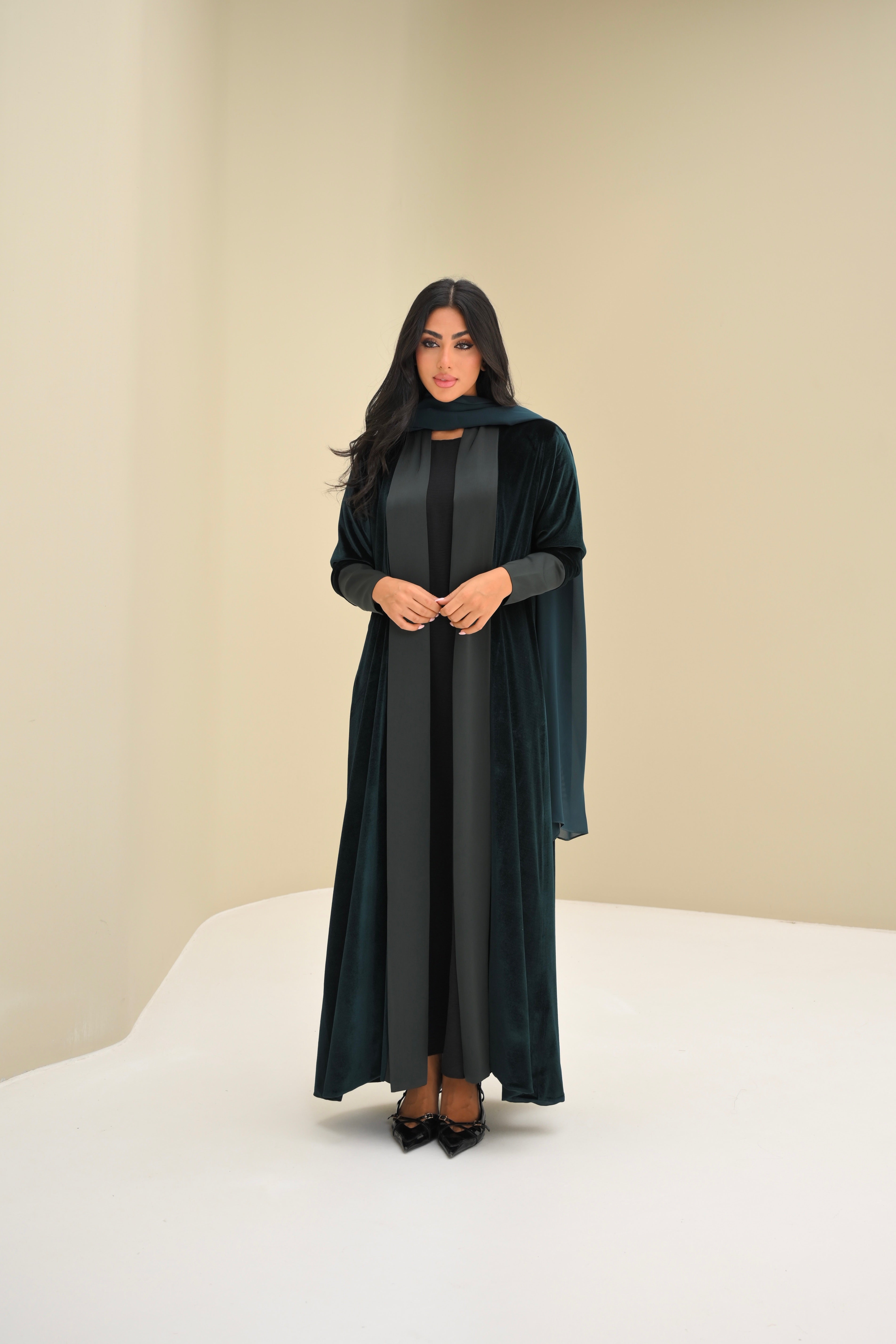 Woman wearing a long dark green dress with a hood against a beige background