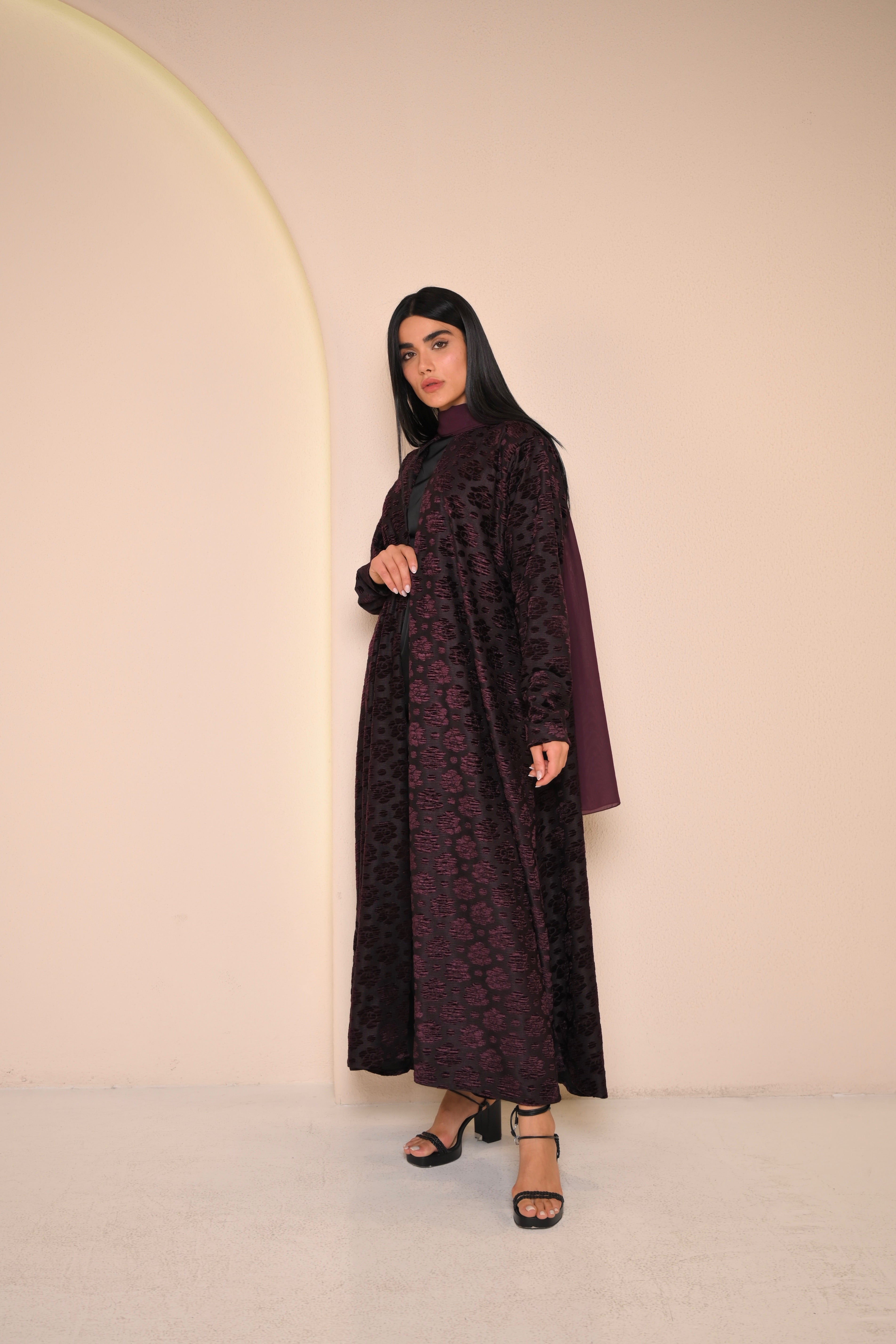 Woman wearing a dark purple dress with a pattern against a plain background
