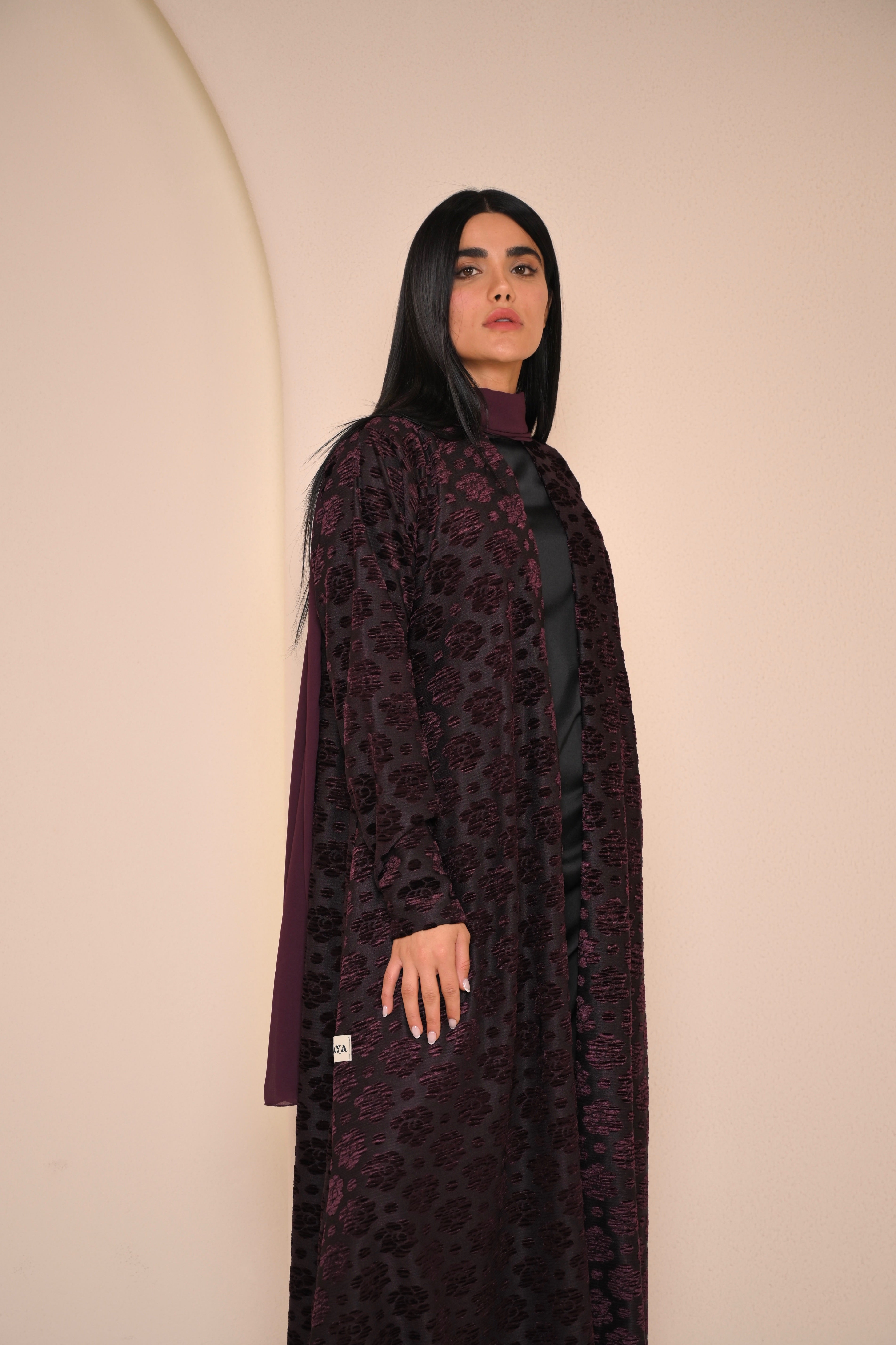 Woman wearing a dark purple dress with a pattern against a beige background