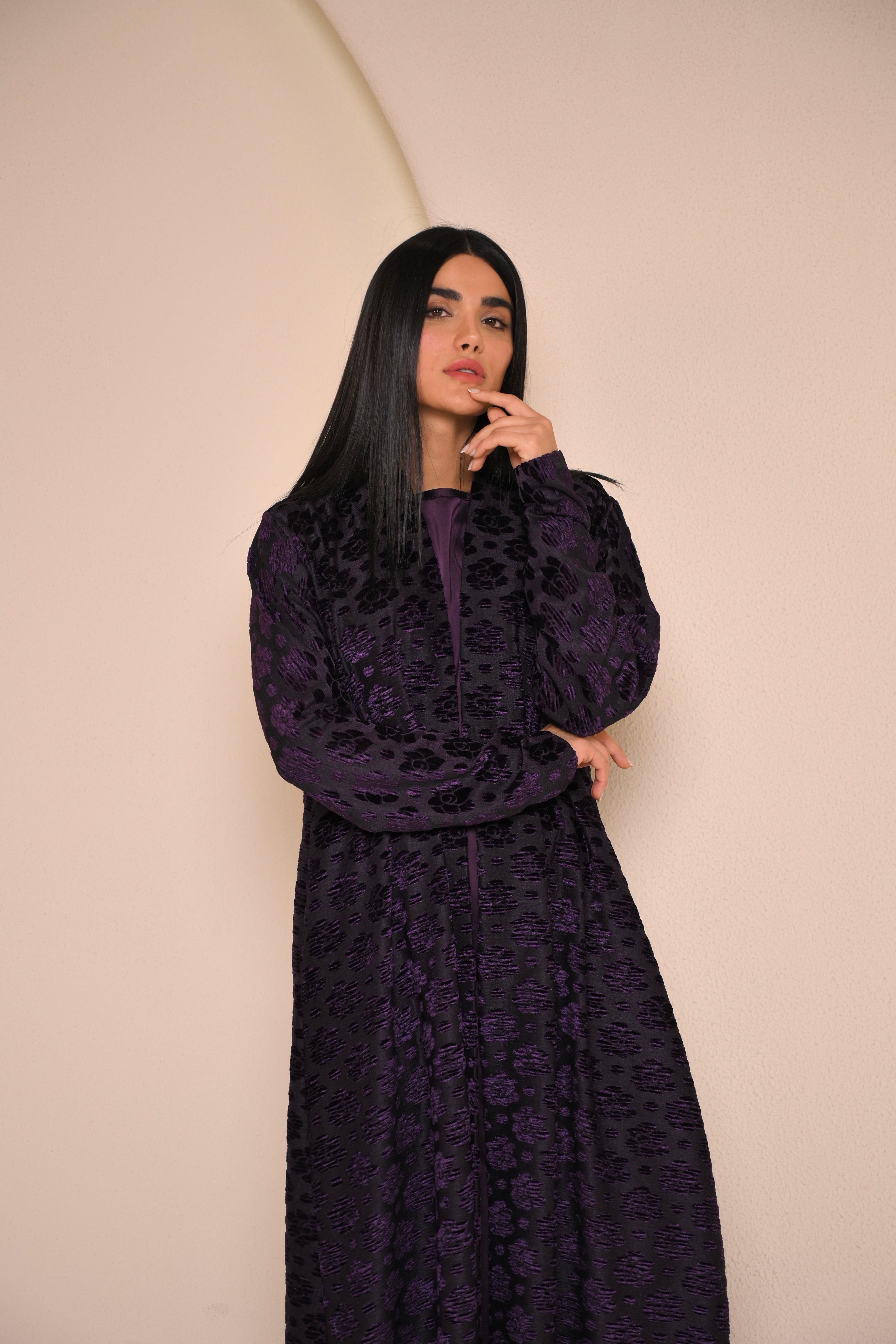 Woman wearing a dark purple dress with a subtle pattern against a beige background