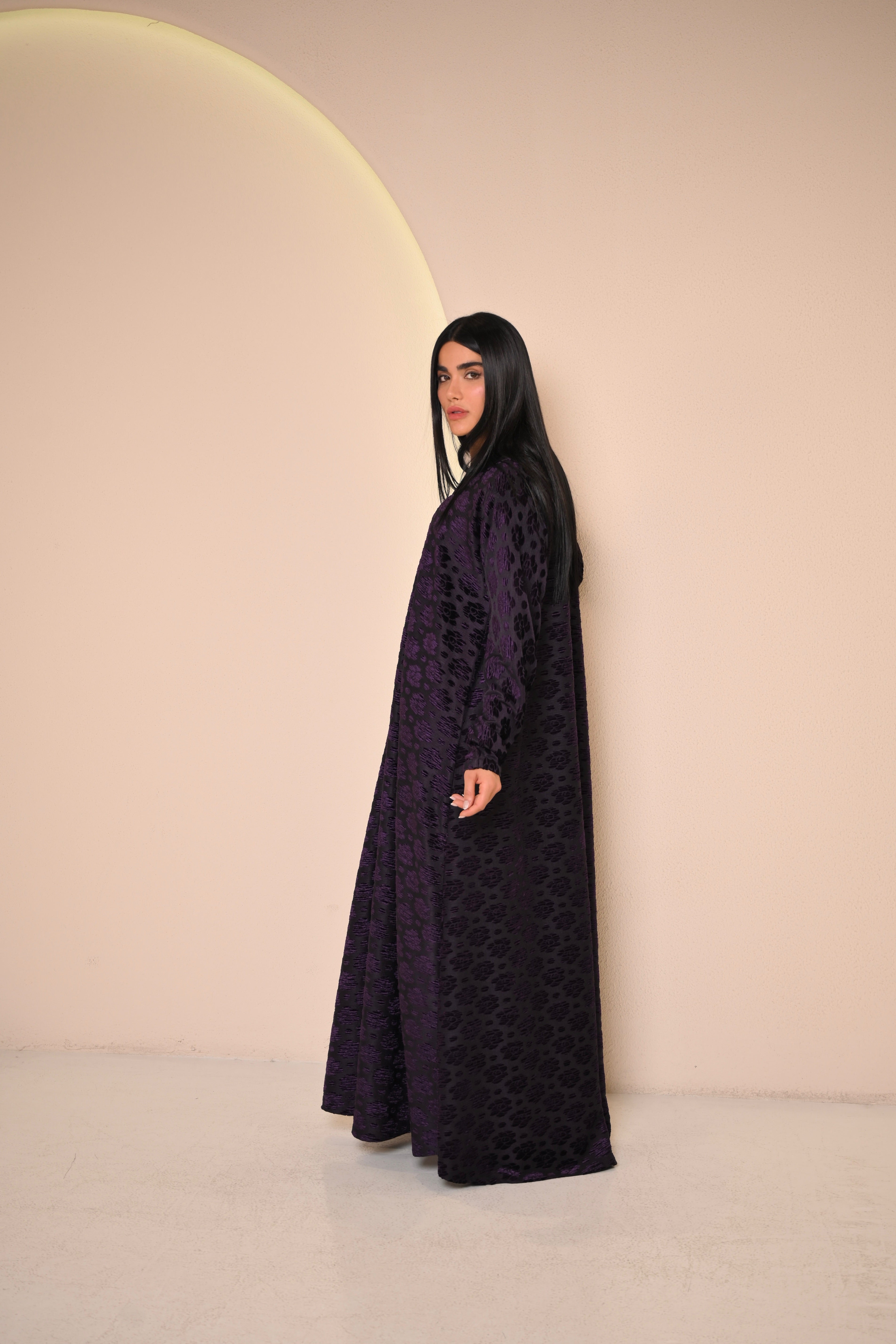 Woman wearing a long dark purple dress with a subtle pattern against a beige background