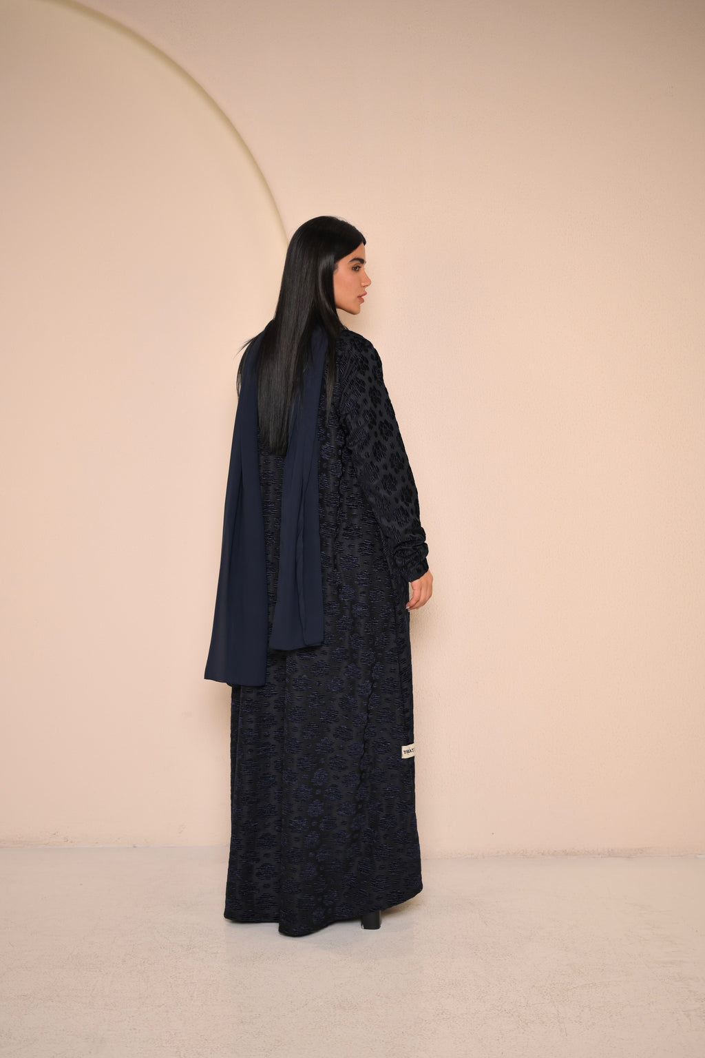 Woman wearing a black lace abaya against a beige background