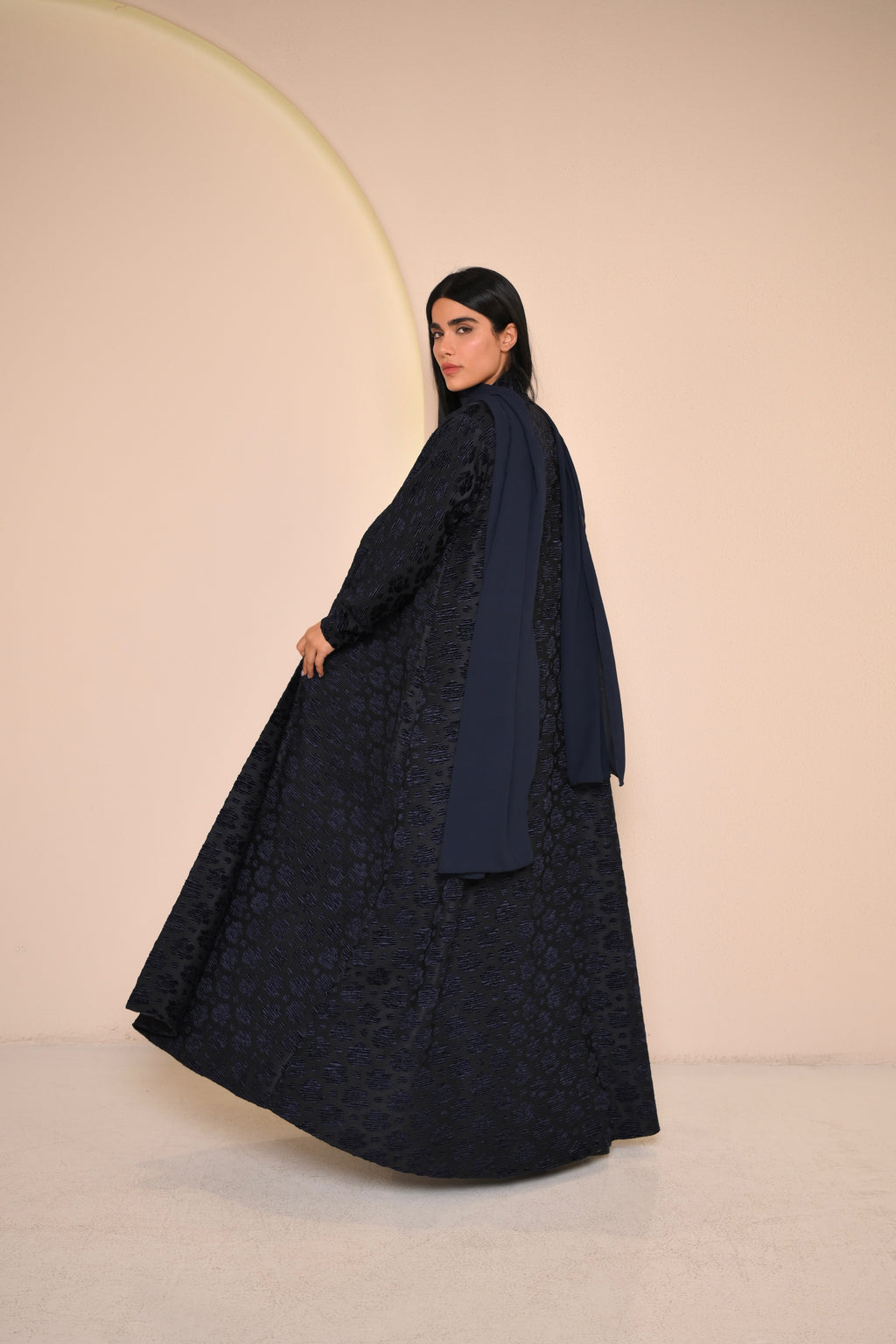 Woman wearing a dark blue lace abaya against a beige background
