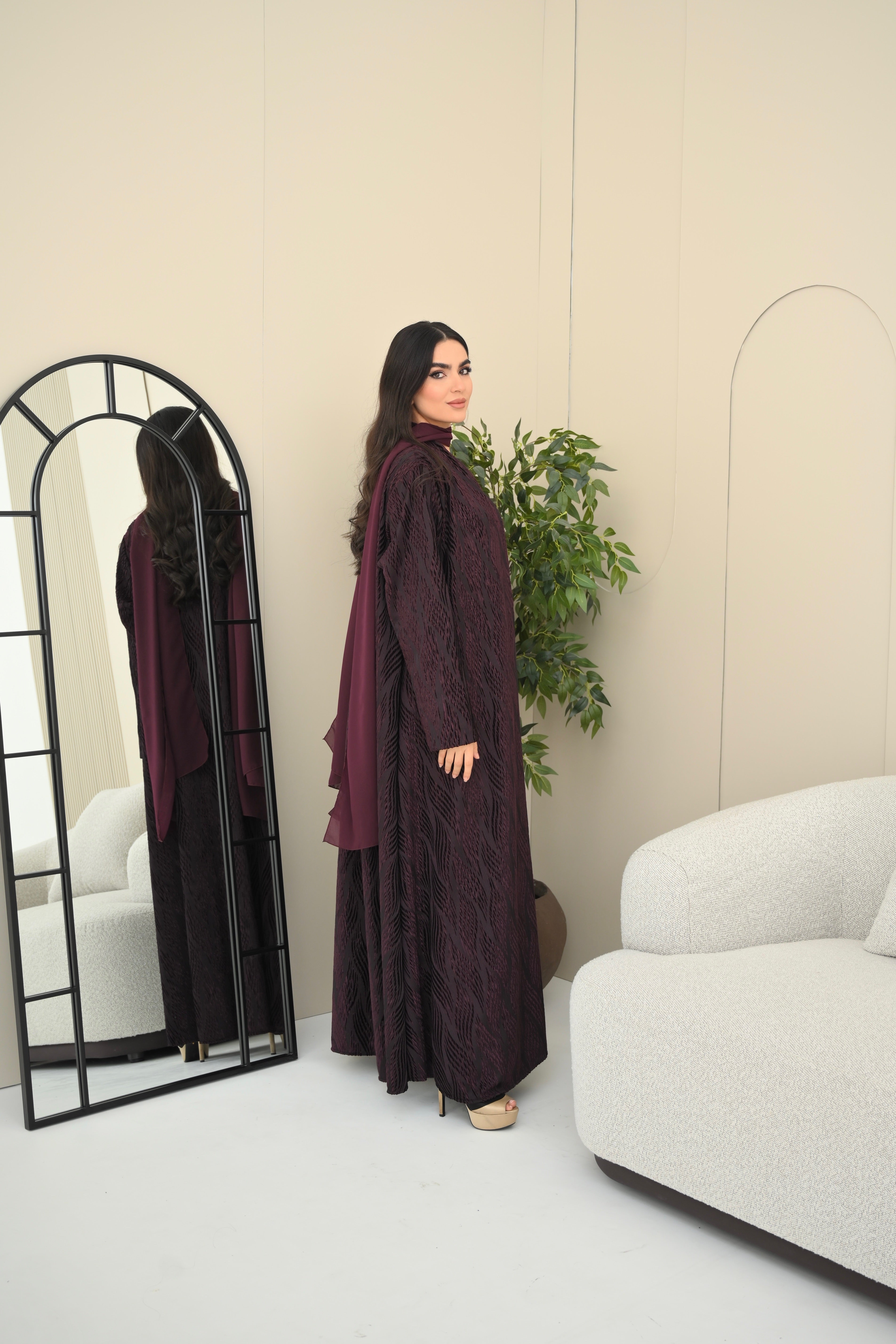 Woman in a dark purple outfit standing in a modern room with a mirror and white sofa.