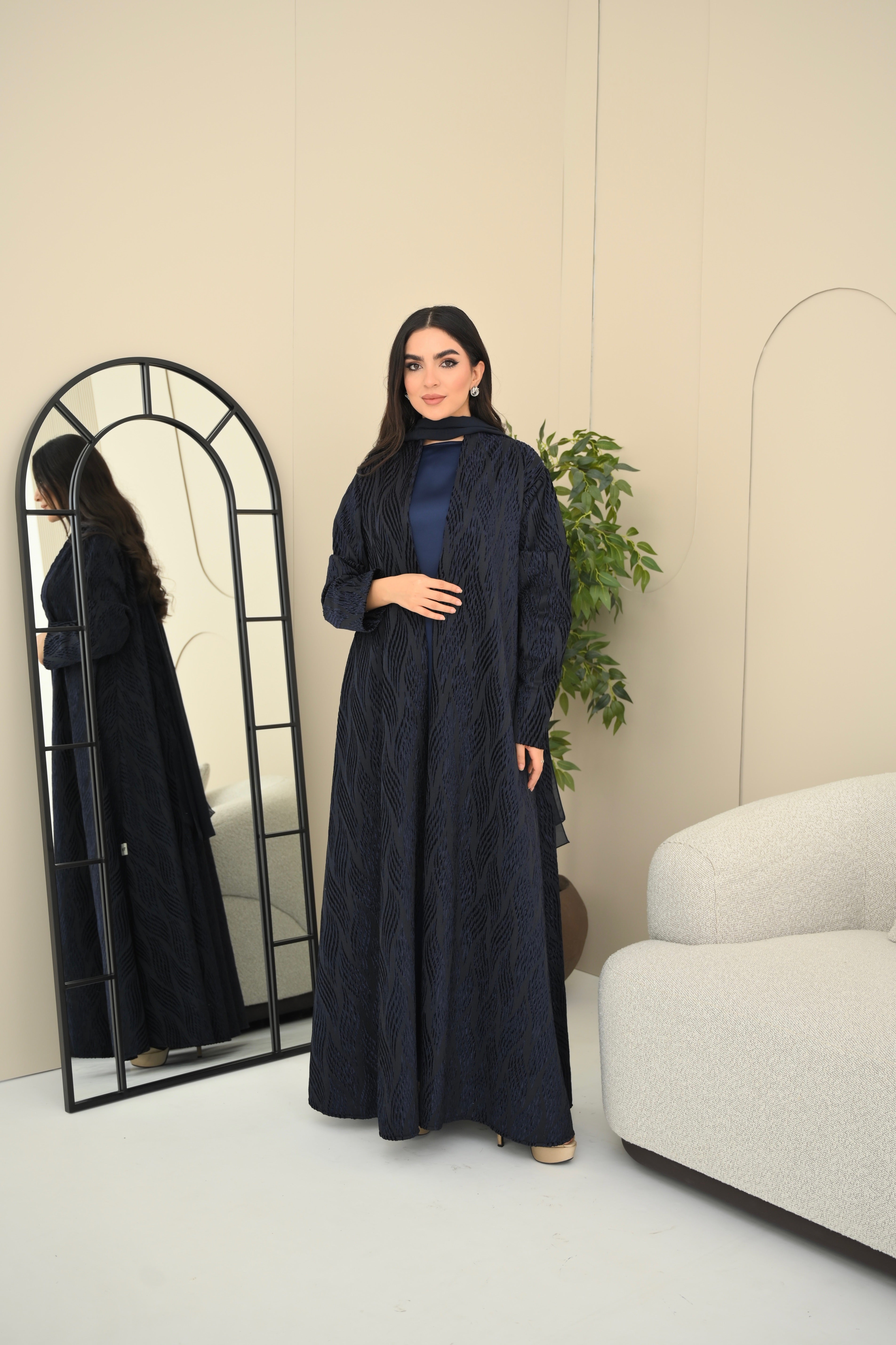 Woman in a long dark blue dress standing in a room with a mirror and plant.