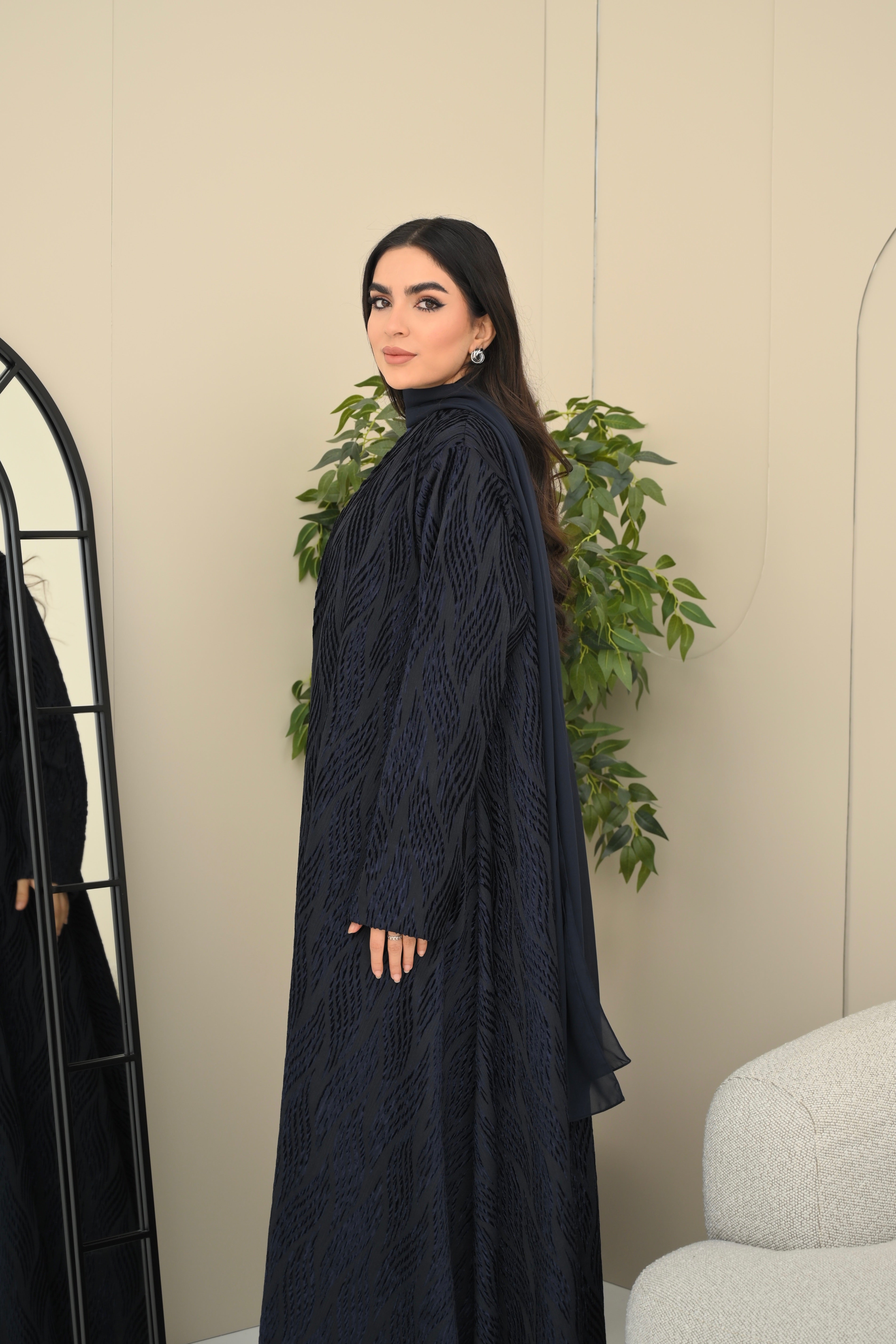 Woman wearing a dark blue dress standing in a room with a mirror and plant.