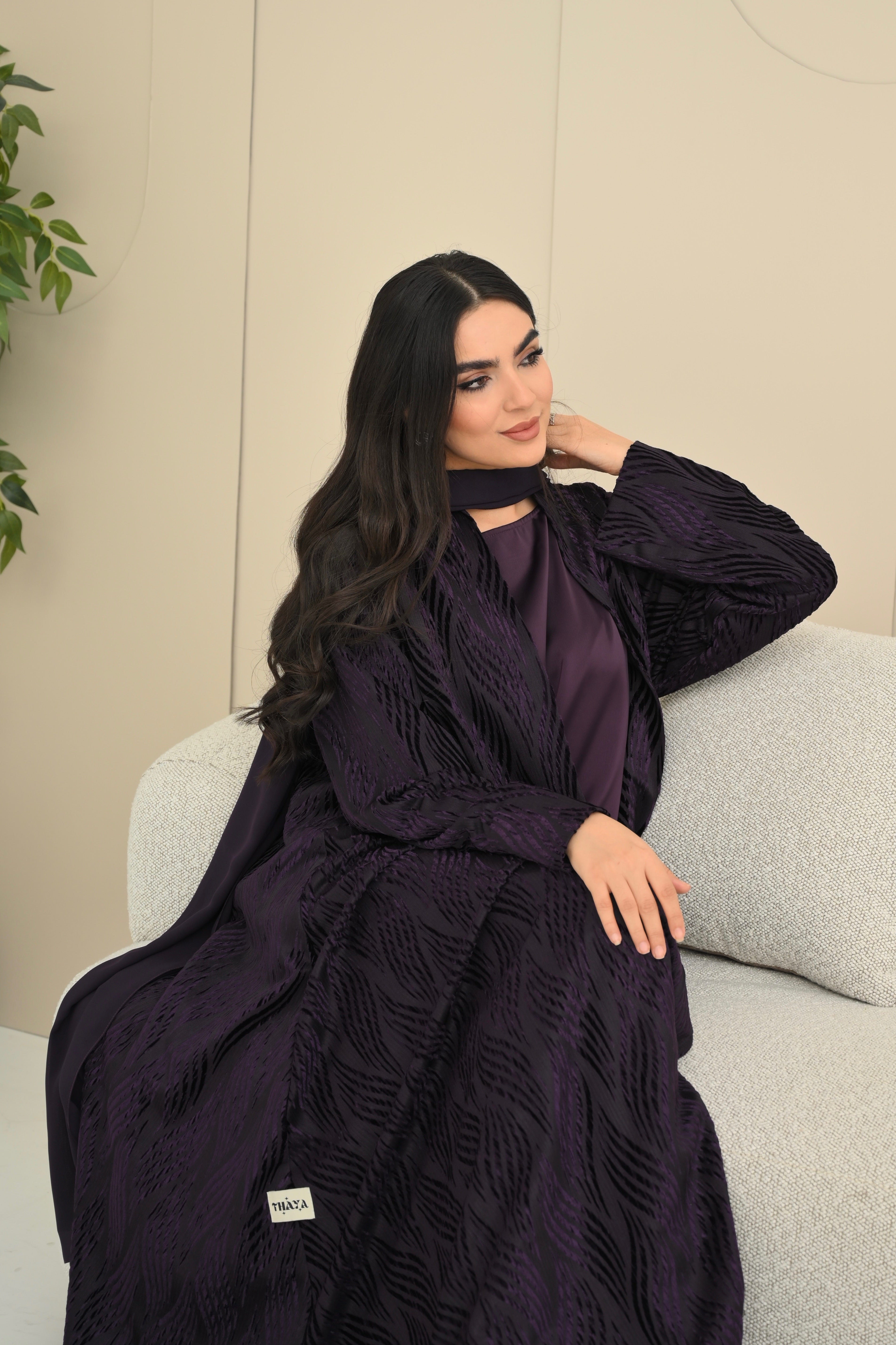 Woman wearing a dark purple outfit sitting on a light-colored couch.