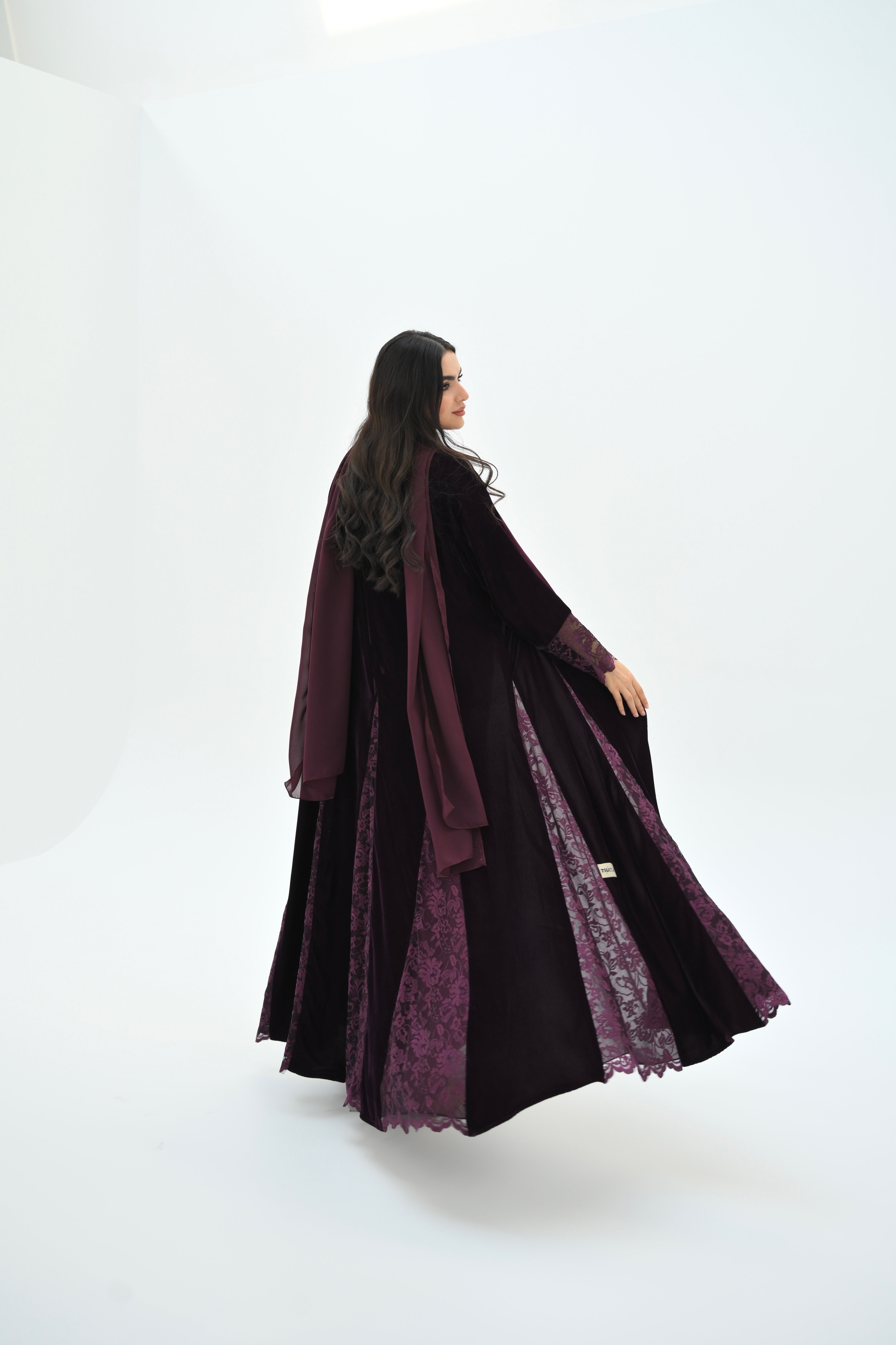 Woman wearing a long, dark purple dress with lace details on a white background