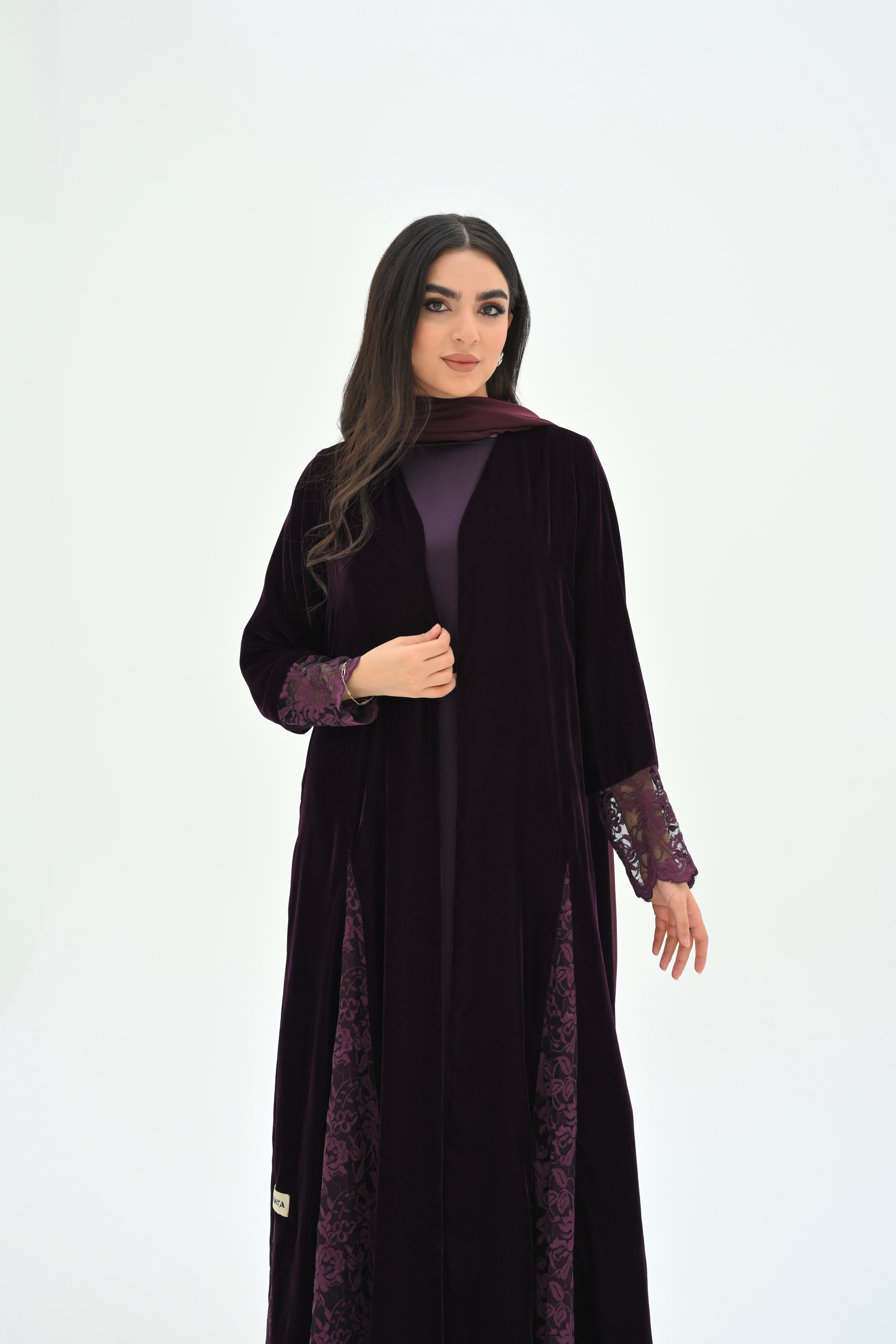 Woman wearing a black abaya with purple accents on a white background