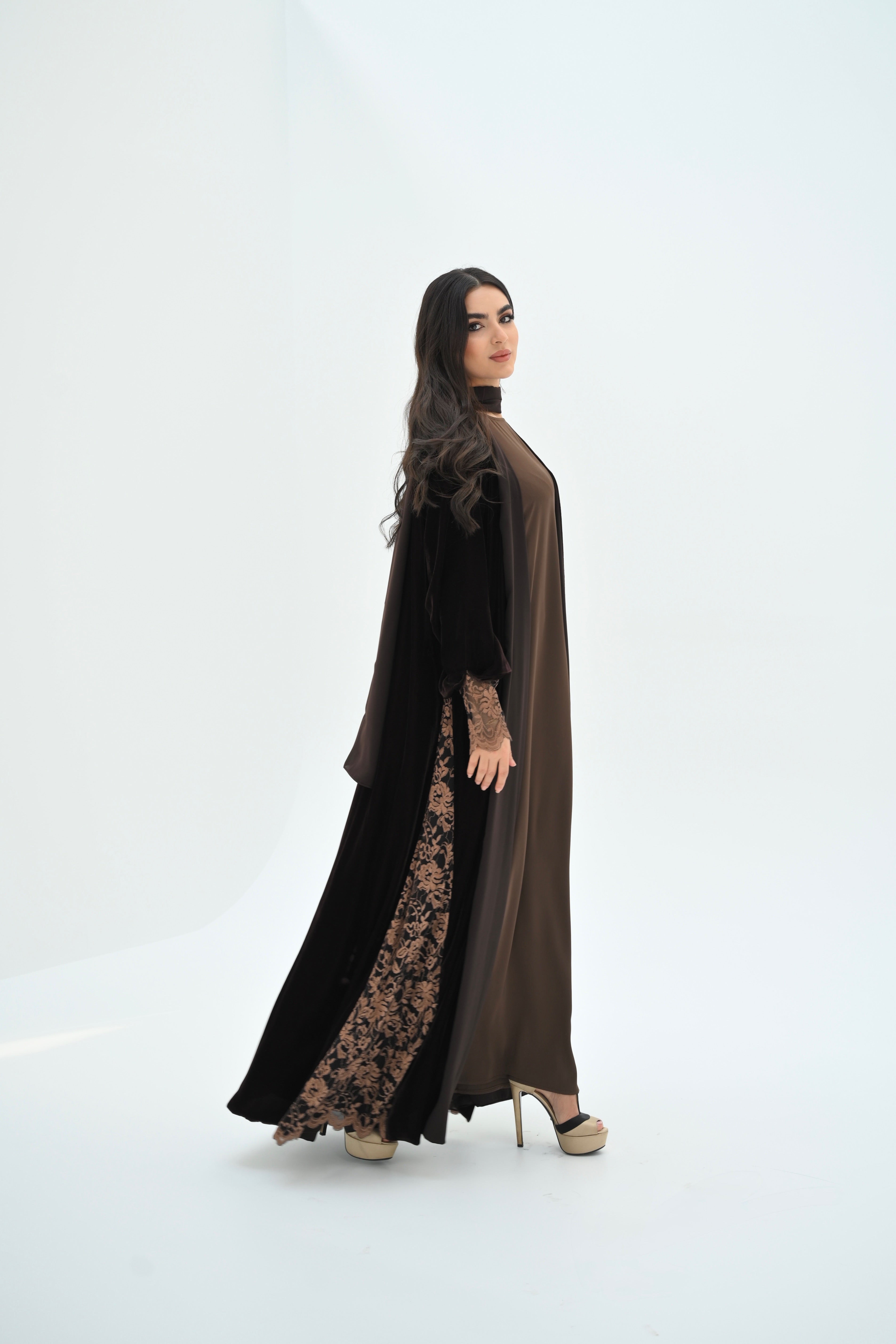 Woman wearing a long, dark brown dress with lace details on a white background
