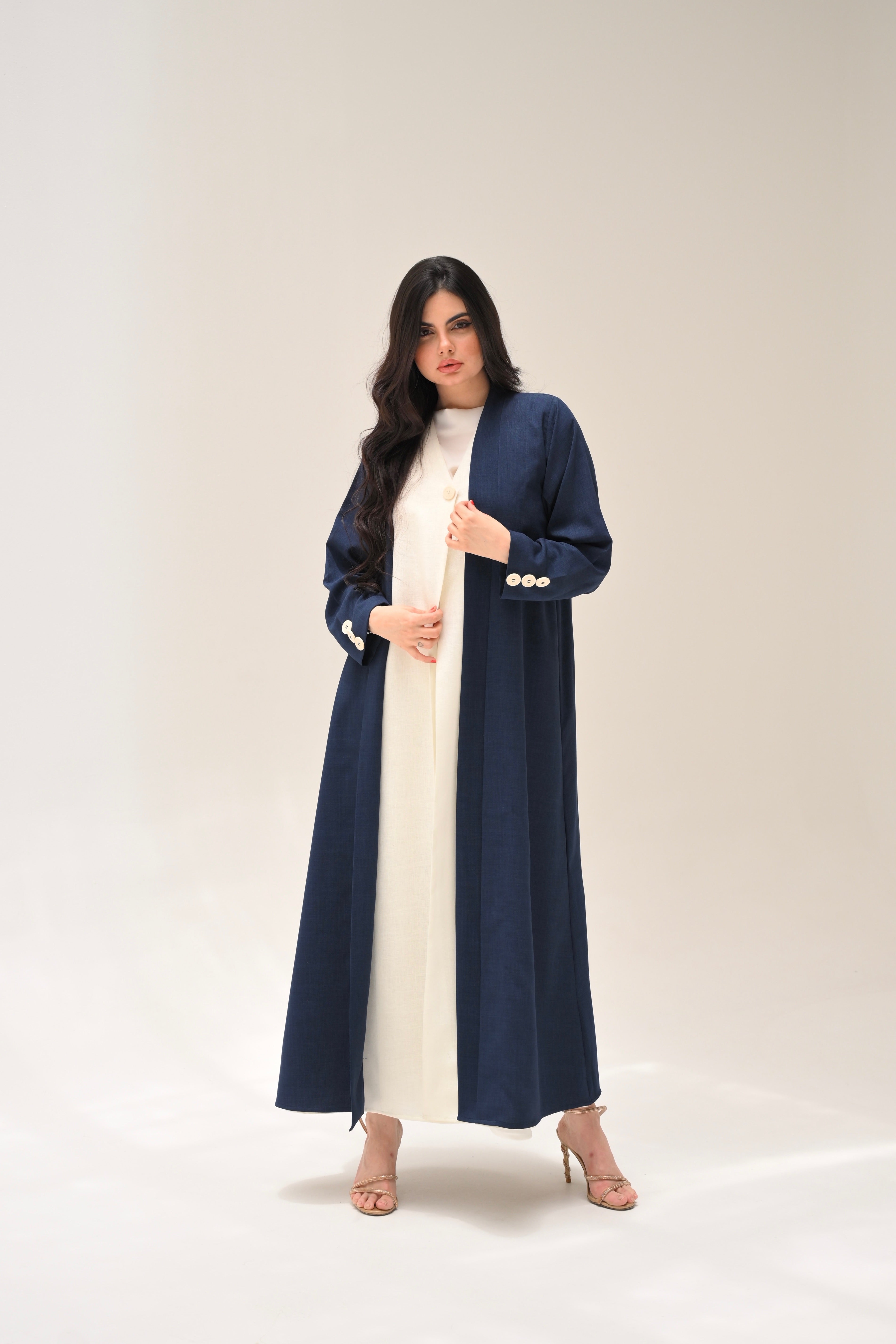 Woman wearing a long navy coat over a white dress on a plain background