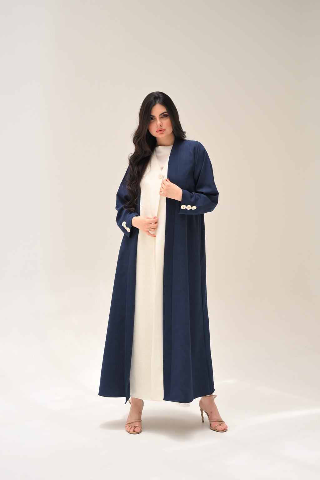 Woman wearing a long navy coat over a white dress on a plain background