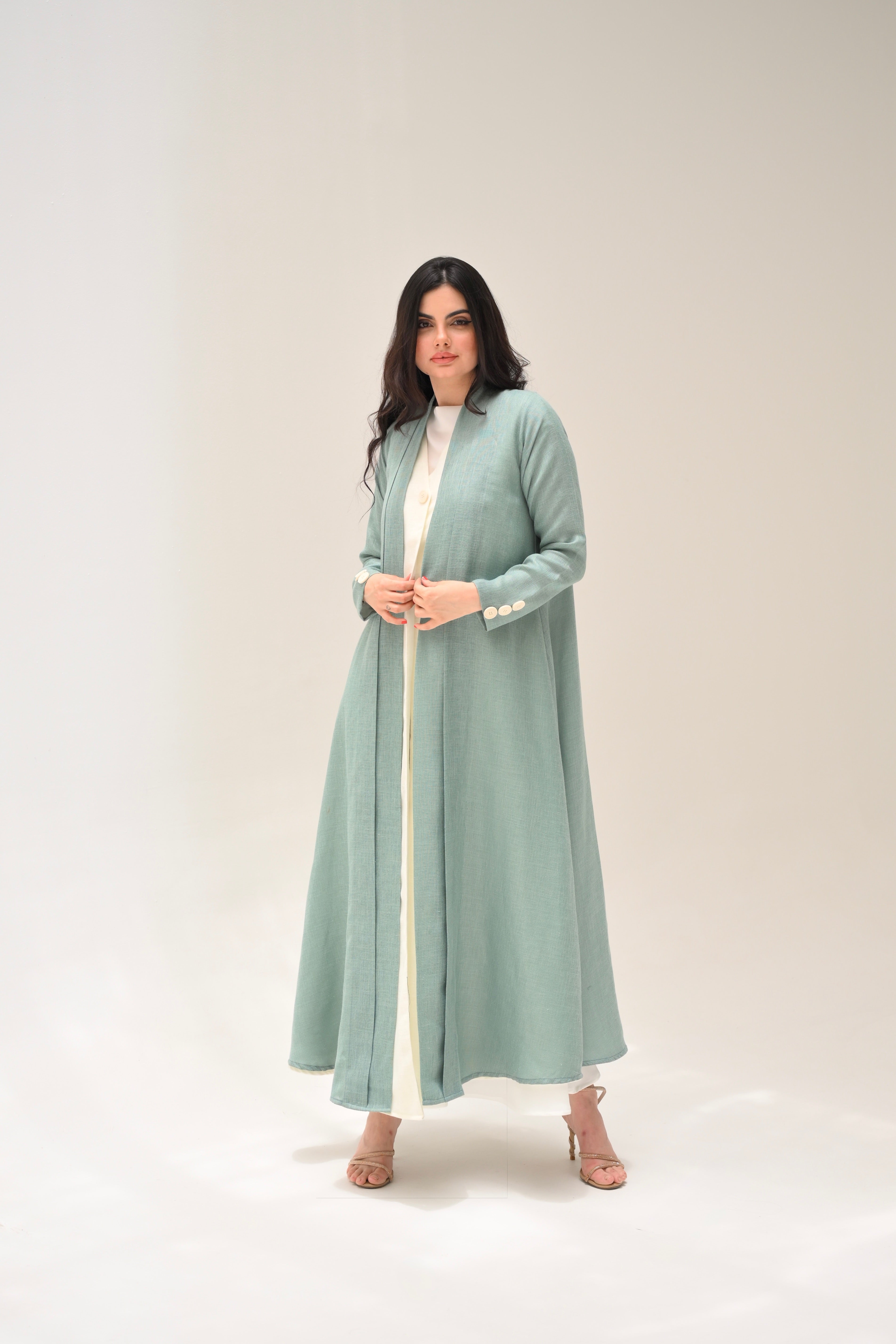 Woman wearing a long light green dress with a white belt on a plain background