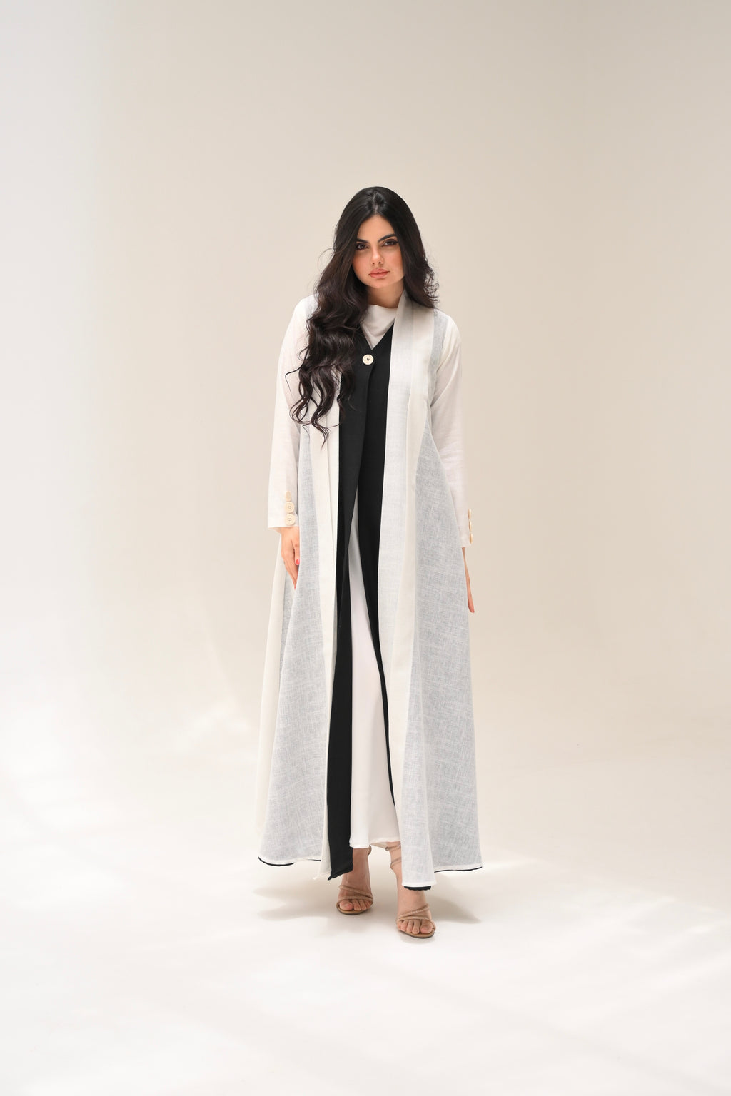 Woman wearing a long white coat over a black and white dress on a plain background