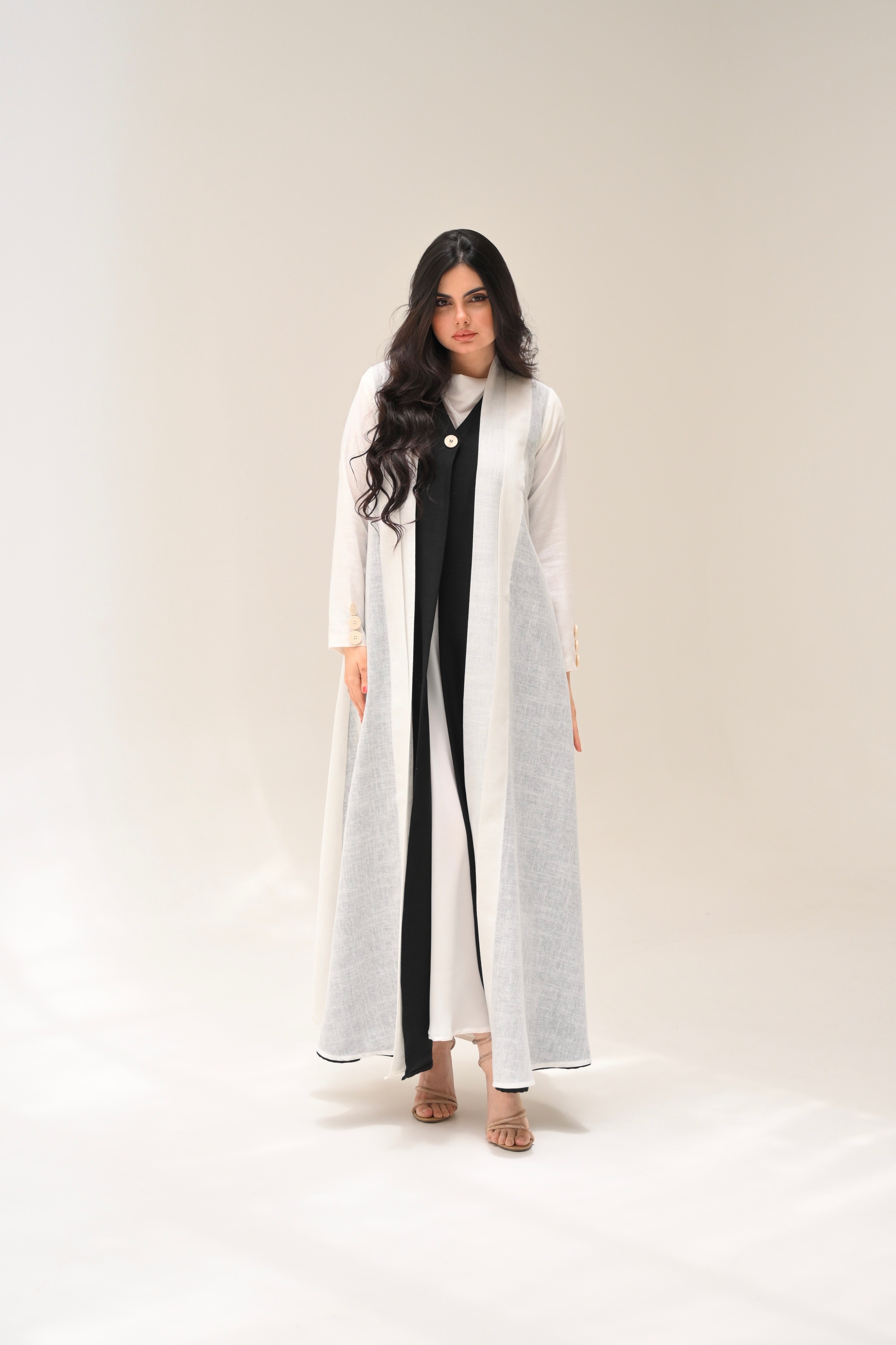 Woman wearing a long white coat over a black and white dress on a plain background