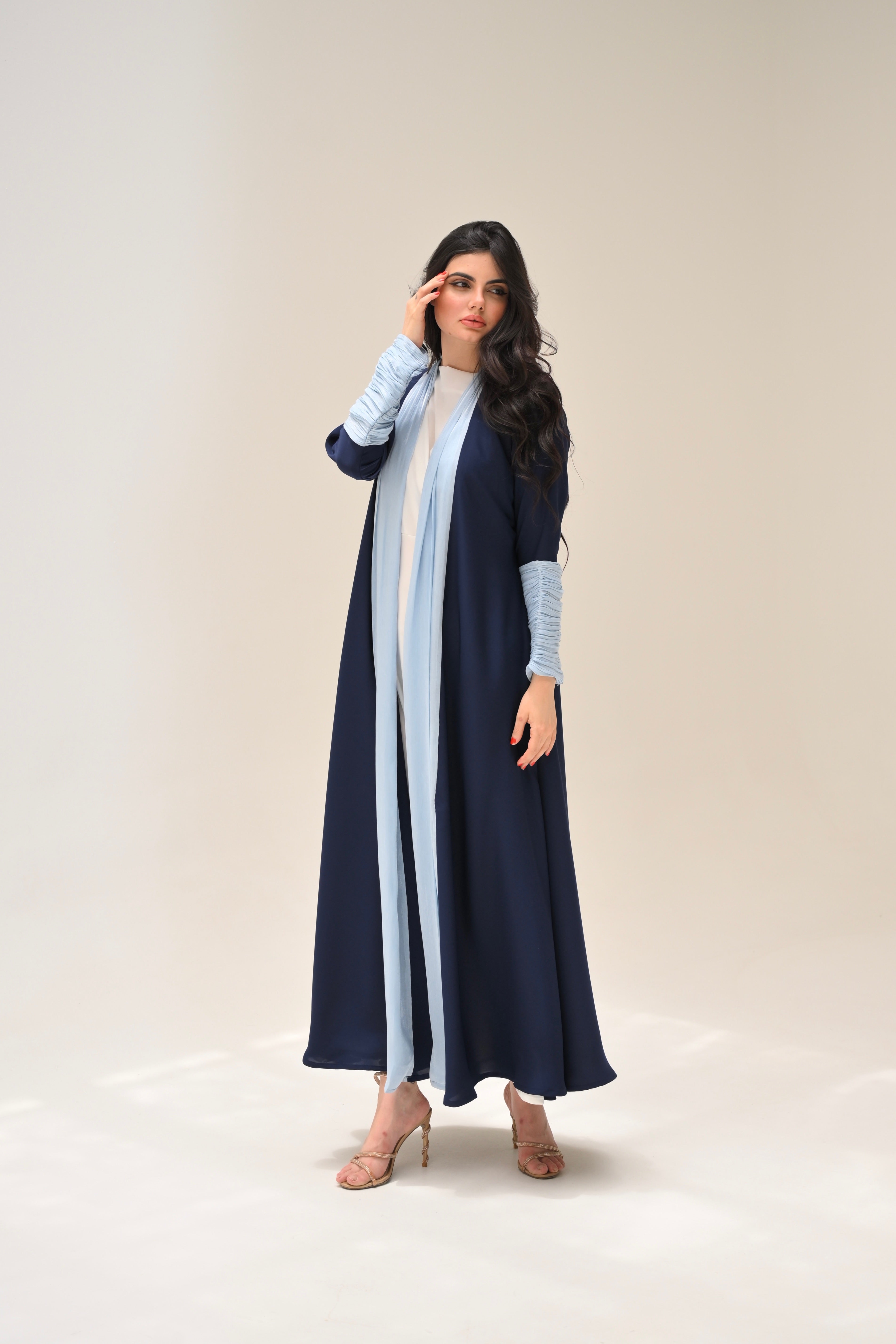 Woman wearing a long navy blue dress with light blue sleeves and a white panel on a beige background