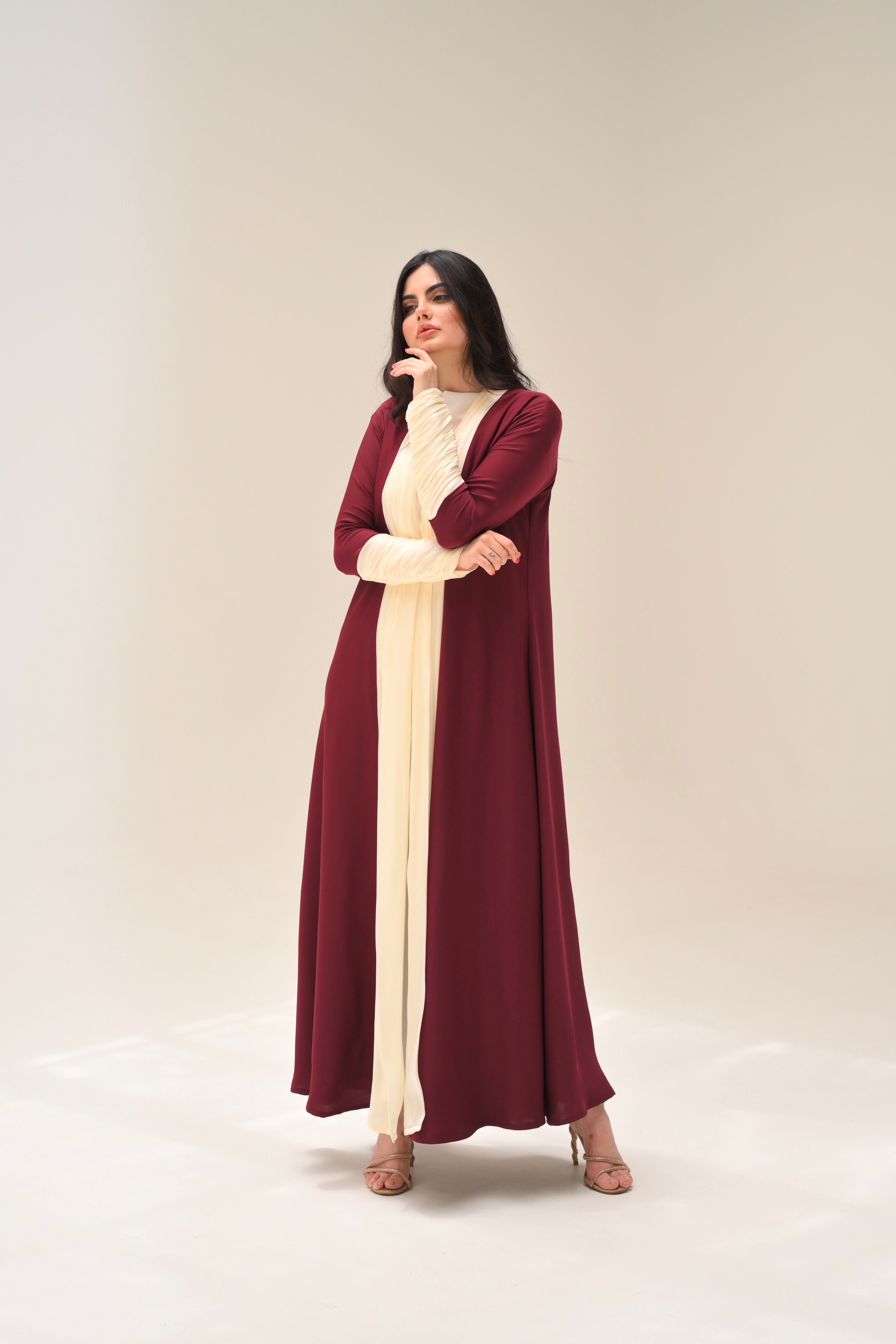 Woman wearing a long, burgundy dress with a cream-colored panel on a white background