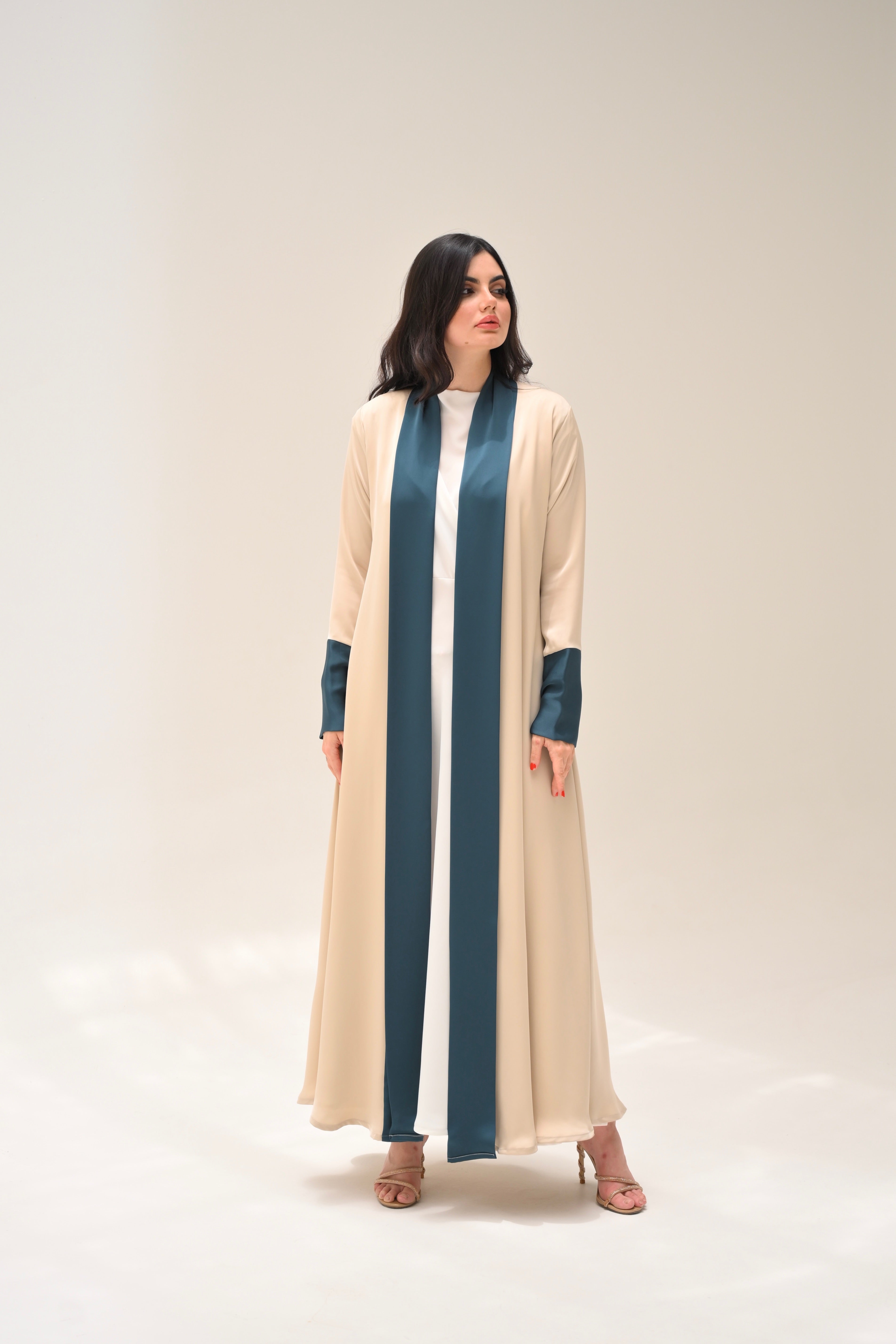 Woman wearing a long, light-colored dress with dark green accents on a white background