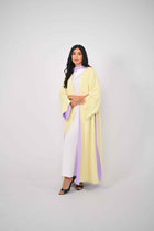 Woman wearing a light yellow and white outfit with a purple accent on a gray background